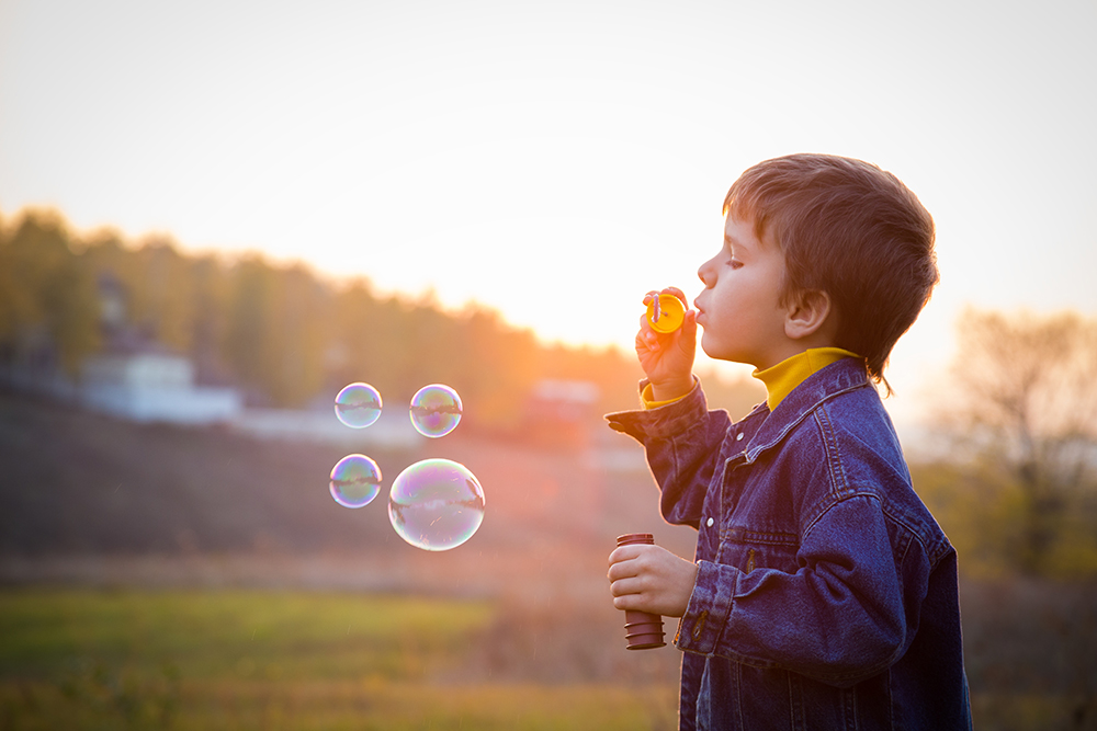 Un niño sopla burbujas en un campo.