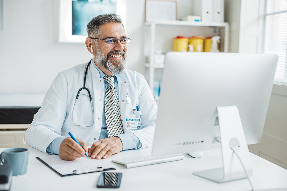 Un médico trabaja en su computadora mientras toma notas.