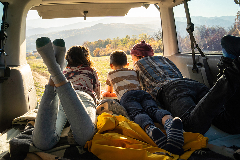 Una familia, en la parte trasera de un coche, mirando hacia la vista de la montaña.