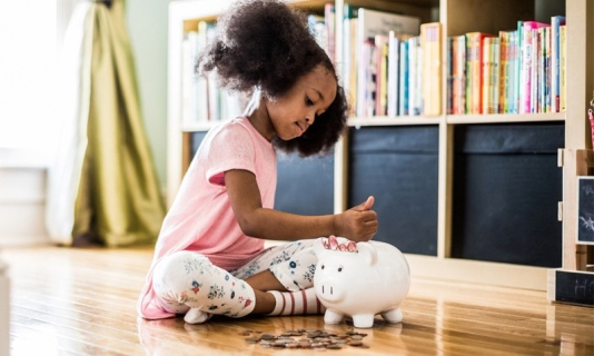 Niña guardando dinero en una alcancía.