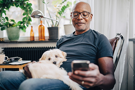 Un hombre mayor afroamericano revisa su teléfono mientras sostiene un perro en su regazo.