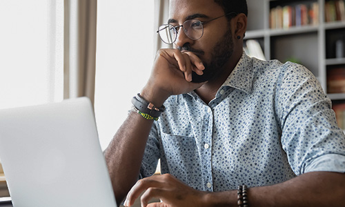 Man sitting at an open laptop, thinking