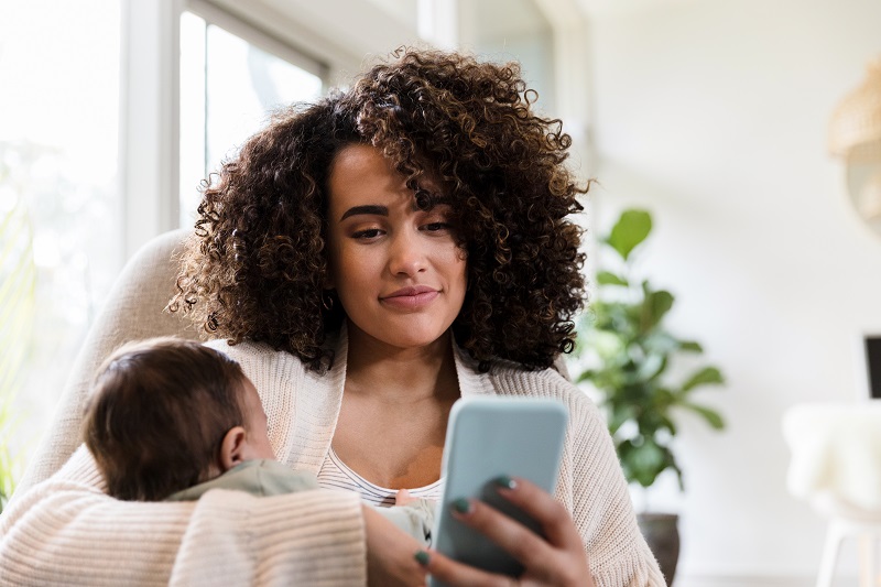 Woman holding a newborn while looking at her phone